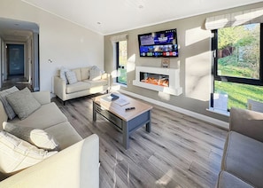 Un salon moderne avec un canapé, une table basse, une cheminée, un téléviseur et une vue sur l’extérieur.