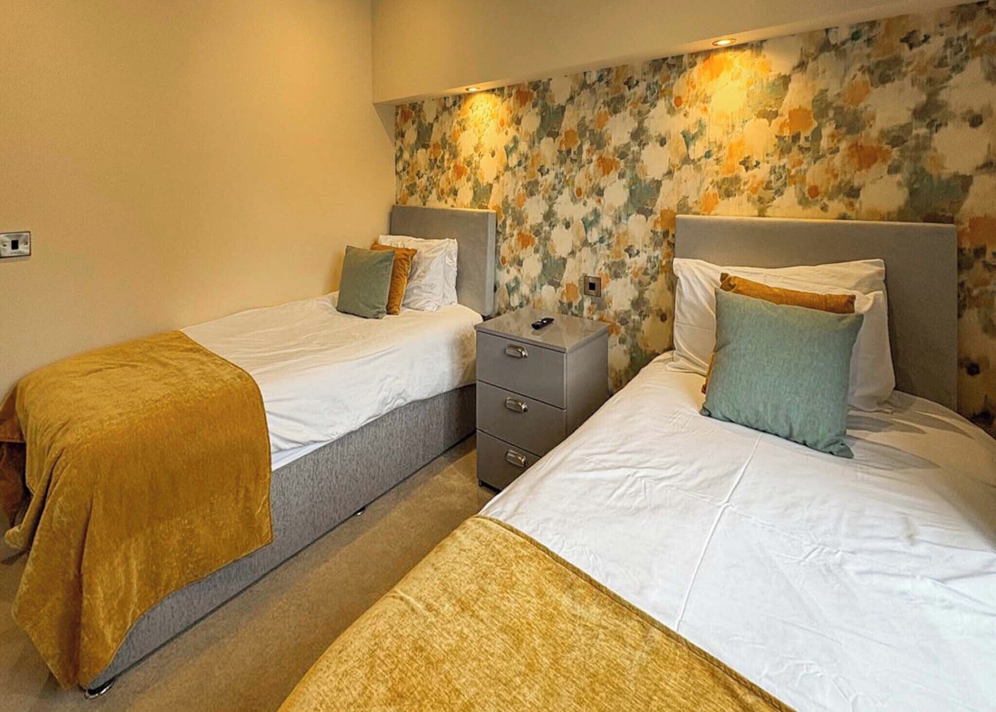 A hotel room with two beds, a nightstand, and a floral-patterned wall.