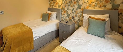 A hotel room with two beds, a nightstand, and a floral-patterned wall.
