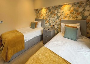 A hotel room with two beds, a nightstand, and a floral-patterned wall. - 3 bedroom accommodation in Faringdon (Faringdon)