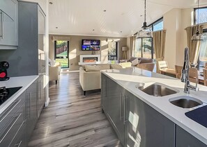 Une cuisine moderne dotée d’un îlot central, un coin repas avec un téléviseur et un salon avec une cheminée.