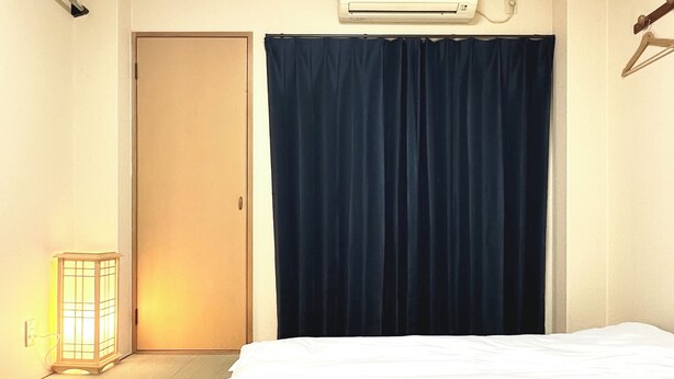 A hotel room with a bed, a nightstand, a wall-mounted air conditioner, and a door. - 2 min walk from Hanazonomachi station Japanese-style room with mini-kitchen with private bathroom Excellent access [ 203]. (大阪市)