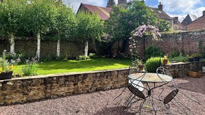 A courtyard with a stone wall, a metal table and chairs, and a view of a church with spires. - Enjoy a cozy setting with a stunning view of the majestic Sées Cathedral. (Sées)