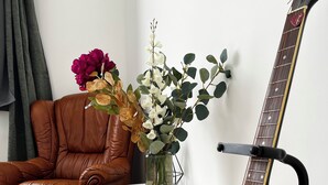 A room with a brown leather chair, a white table, a black guitar, and a vase with flowers. - Enjoy a cozy setting with a stunning view of the majestic Sées Cathedral. (Sées)