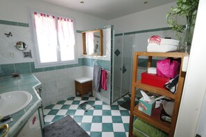 Kylpyhuone, jossa on pesuallas, peili, suihku ja hylly, jossa on hygieniatuotteita.