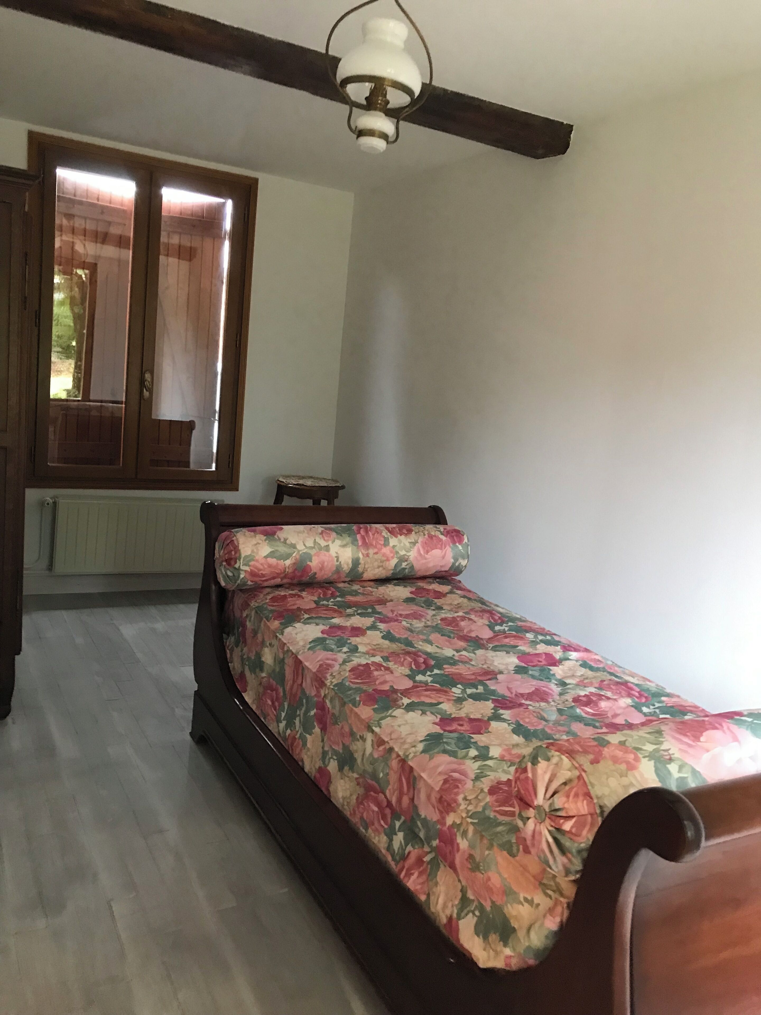 A bedroom with a wooden bed, a window with curtains, a radiator, and a ceiling fan.