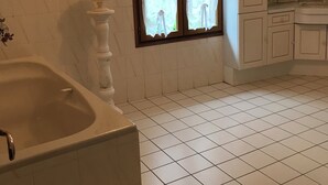 Un bany amb banyera, una finestra amb cortines i un lavabo amb armaris.
