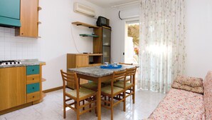 A compact kitchen with a dining table and chairs, a sofa, and a TV on a shelf. - Bright flat with large balcony in Bibione (Bibione)
