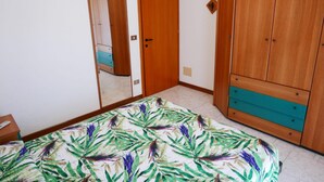 A bedroom with a bed, wooden wardrobe, and a mirror. - Bright flat with large balcony in Bibione (Bibione)