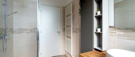 Un baño moderno con cabina de ducha de vidrio, tocador de madera y estante empotrado con plantas en macetas.