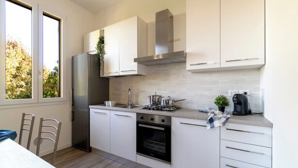 A modern kitchen with white cabinets, a stainless steel refrigerator, a gas stove, and a coffee maker. - Room-charming Guest Room in Frassino wit (Castel San Pietro Terme)