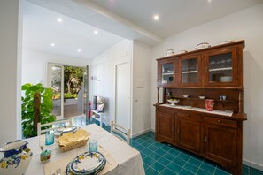 A dining area with a table set for two, a cabinet with glass doors, and a view of the outdoors. - Casa Nostra - Private Sea View Garden (Praiano)