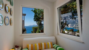 A room with a white sofa, a view of the sea, and a wall with decorative plates. - Casa Nostra - Private Sea View Garden (Praiano)