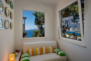 A room with a white sofa, a view of the sea, and a wall with decorative plates. - Casa Nostra - Private Sea View Garden (Praiano)