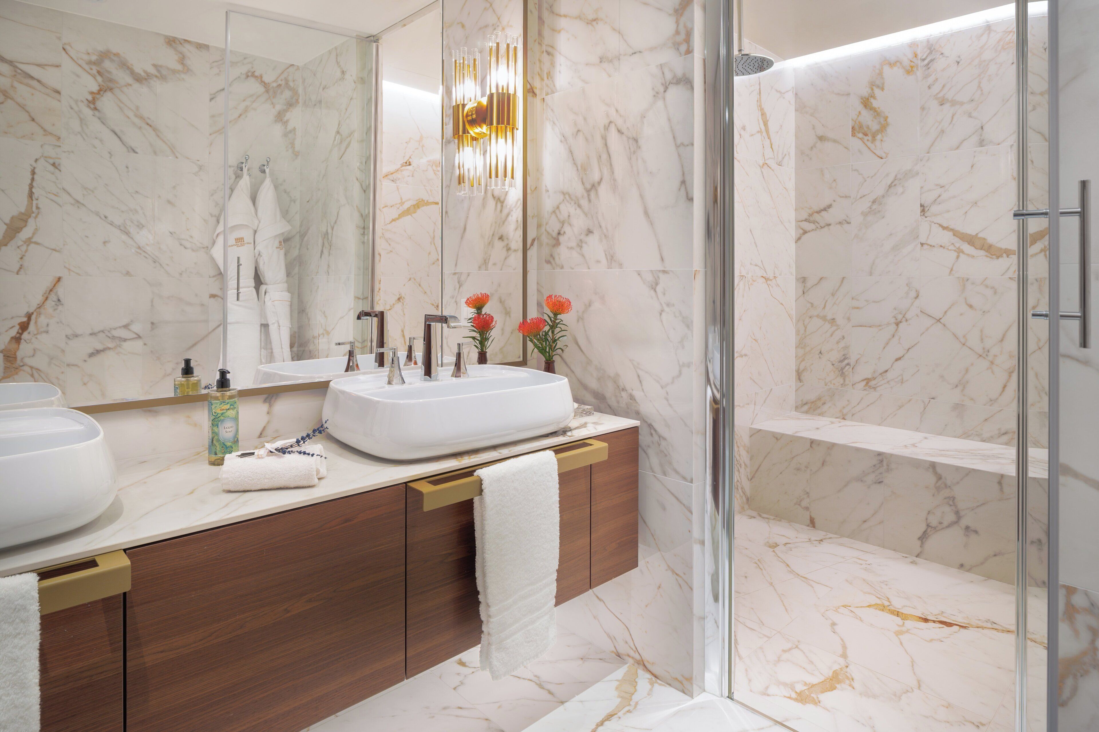 A modern bathroom with marble walls, a large sink, and a glass shower enclosure.