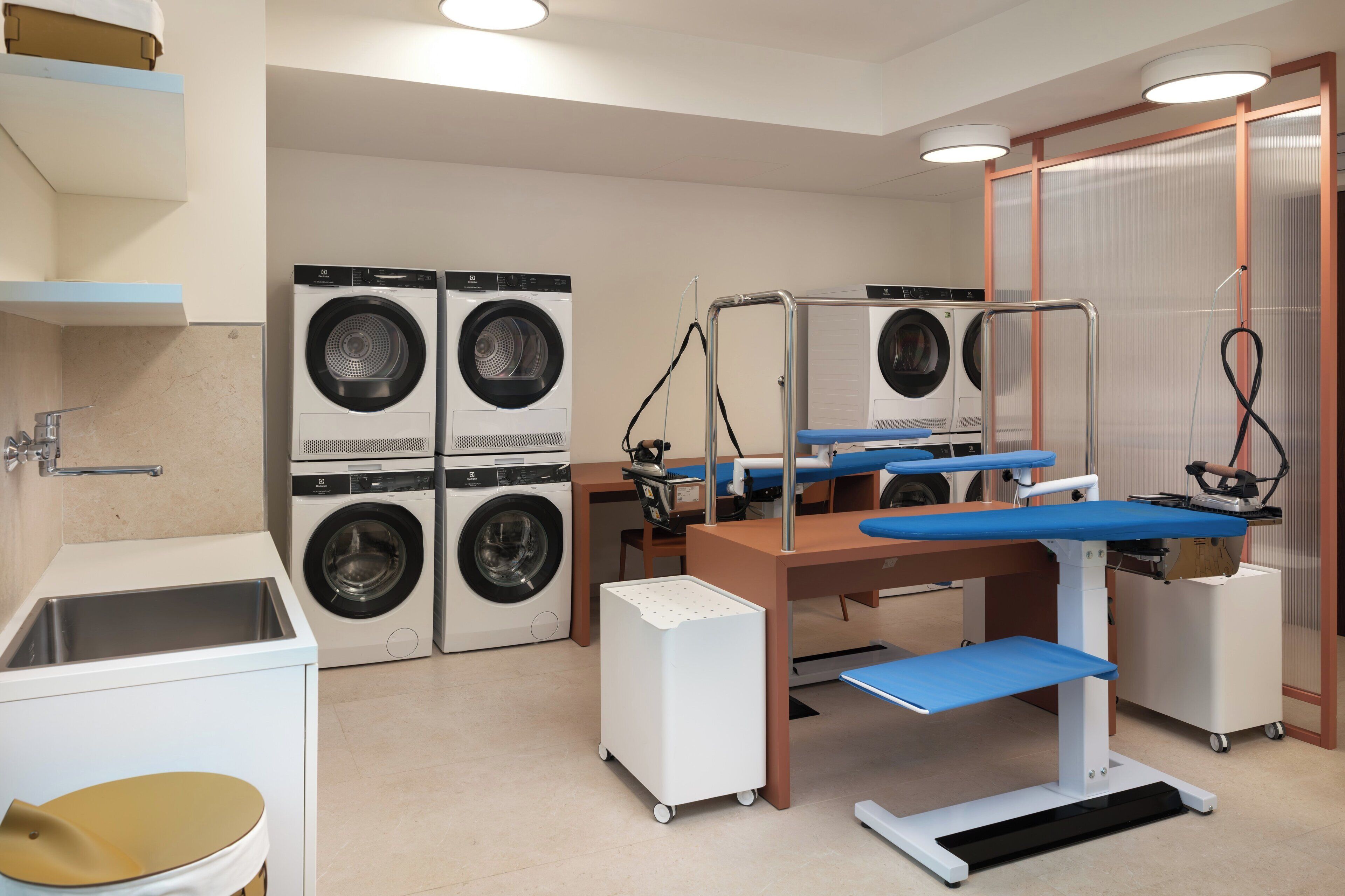 A laundry room with four washing machines, a sink, and a blue bench.