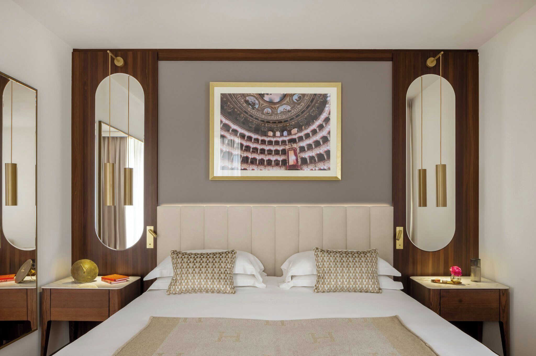 A hotel room with a large bed, two nightstands, a large mirror, and a framed picture of an opera house on the wall.