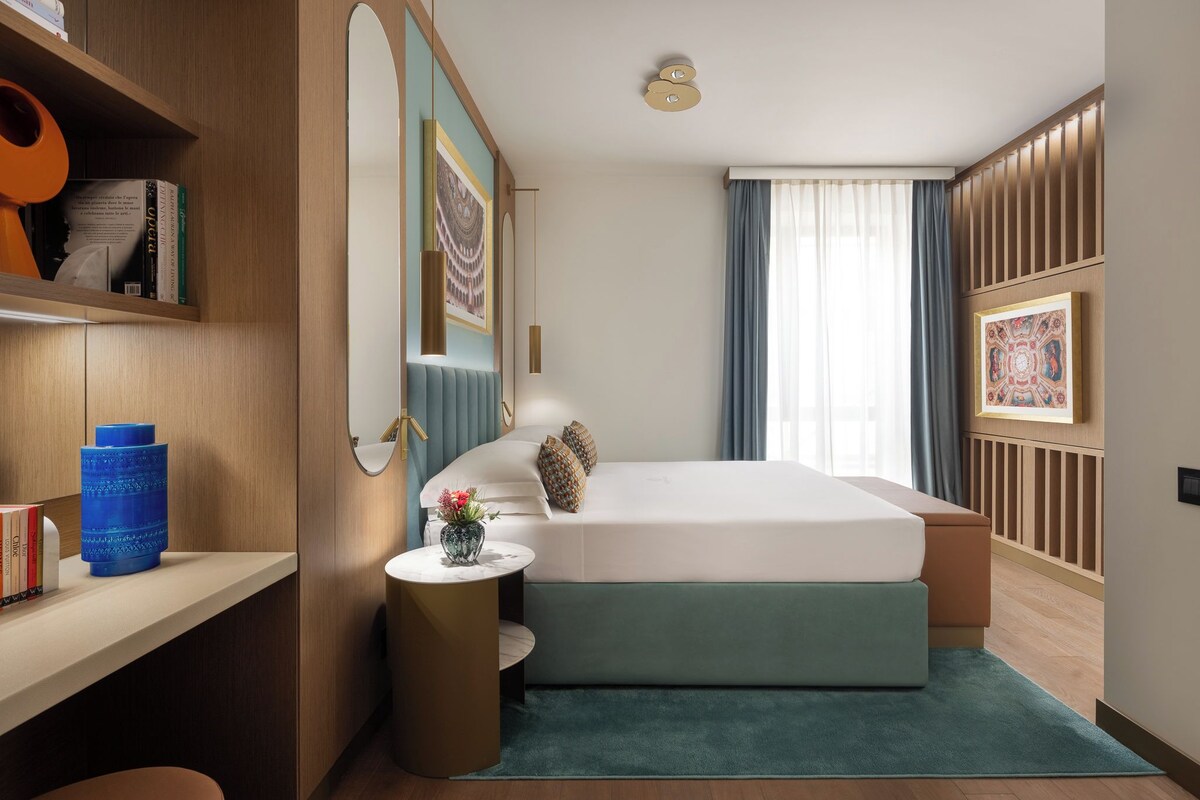 A modern bedroom with a bed, bedside table, and a shelf with books and a vase.