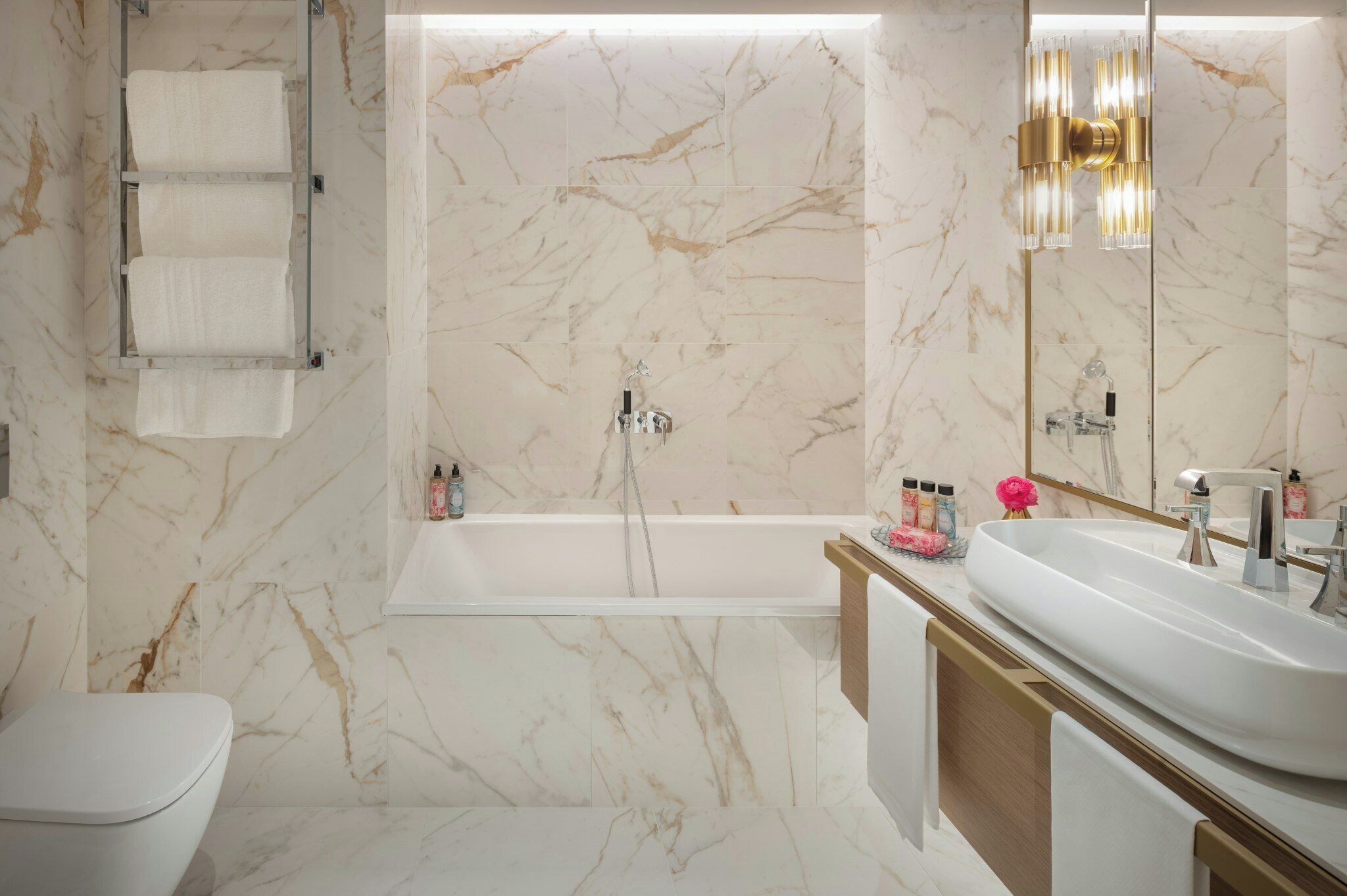 A modern bathroom with a marble wall, a bathtub, a sink, and a toilet.