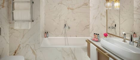 A modern bathroom with a marble wall, a bathtub, a sink, and a toilet.