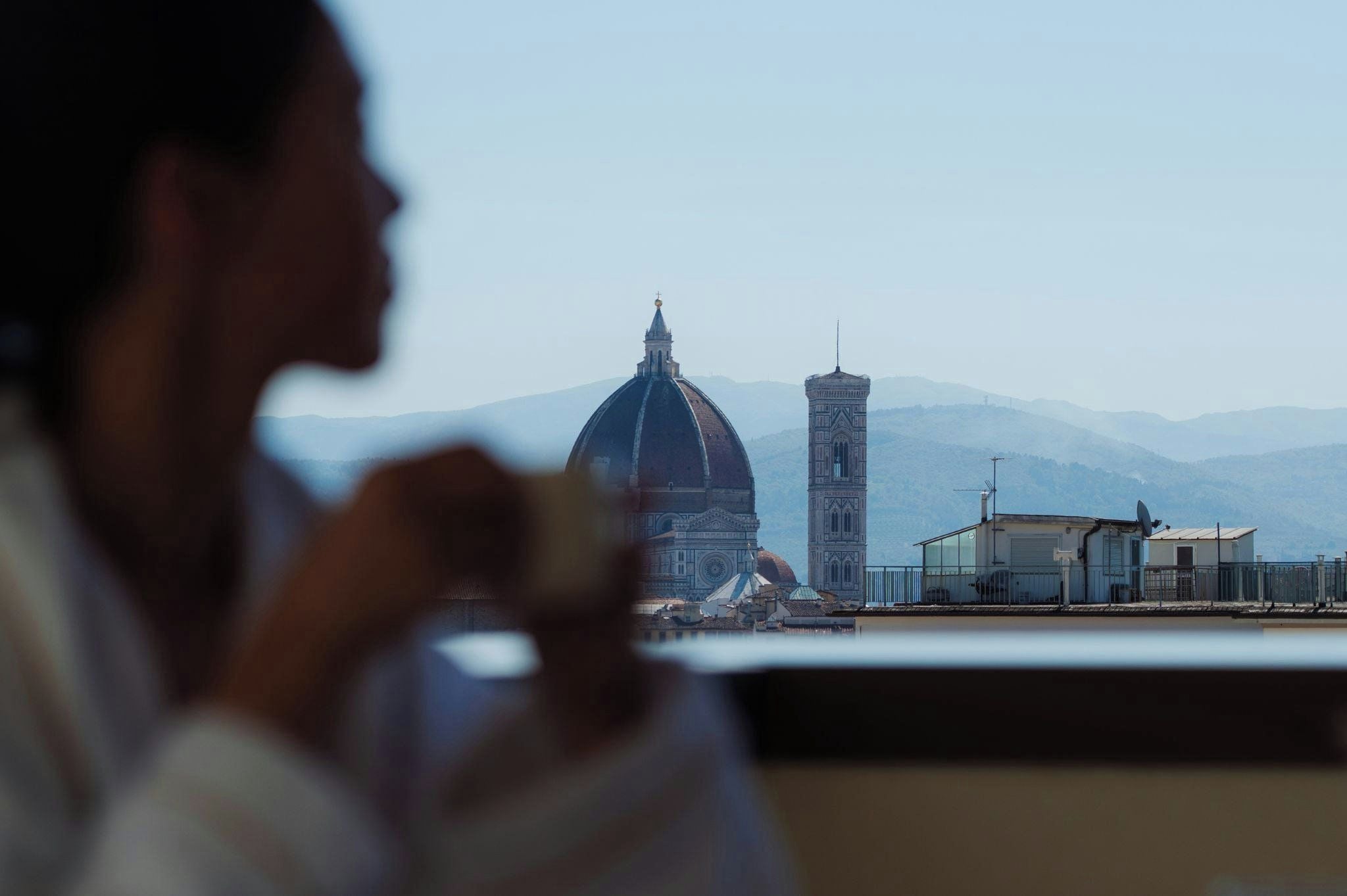 A view of a dome and tower from a balcony overlooking a body of water and mountains.