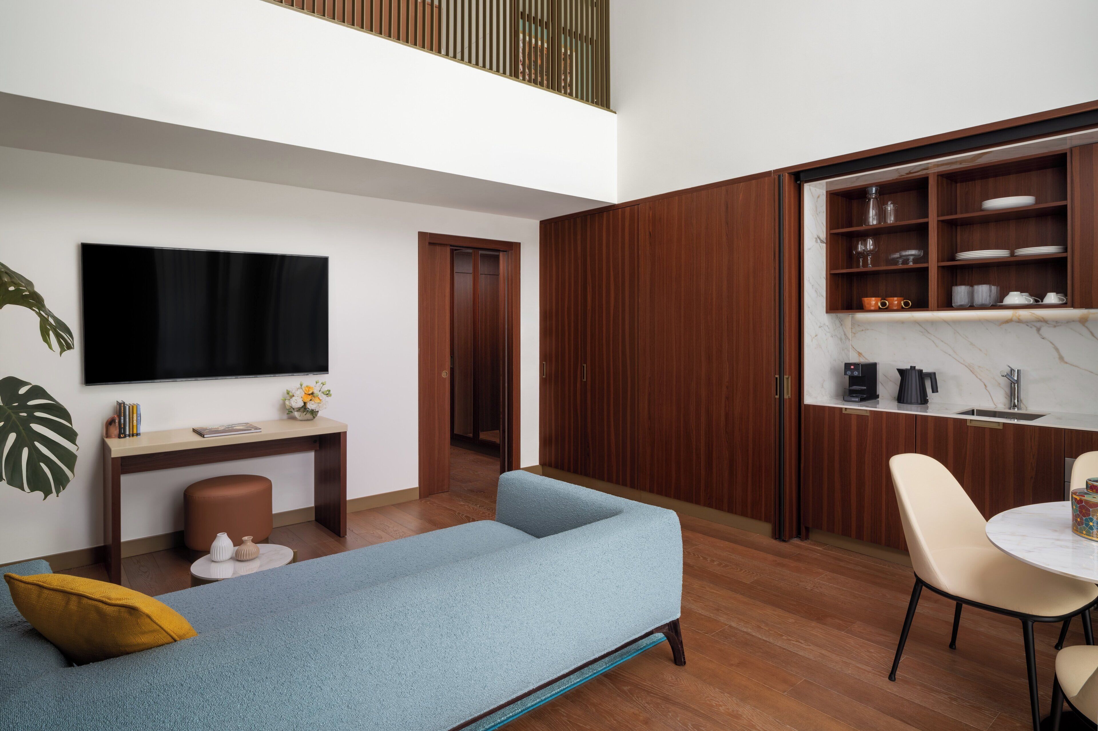 A modern living room with a sofa, a coffee table, a TV, and a dining area with chairs and a table.