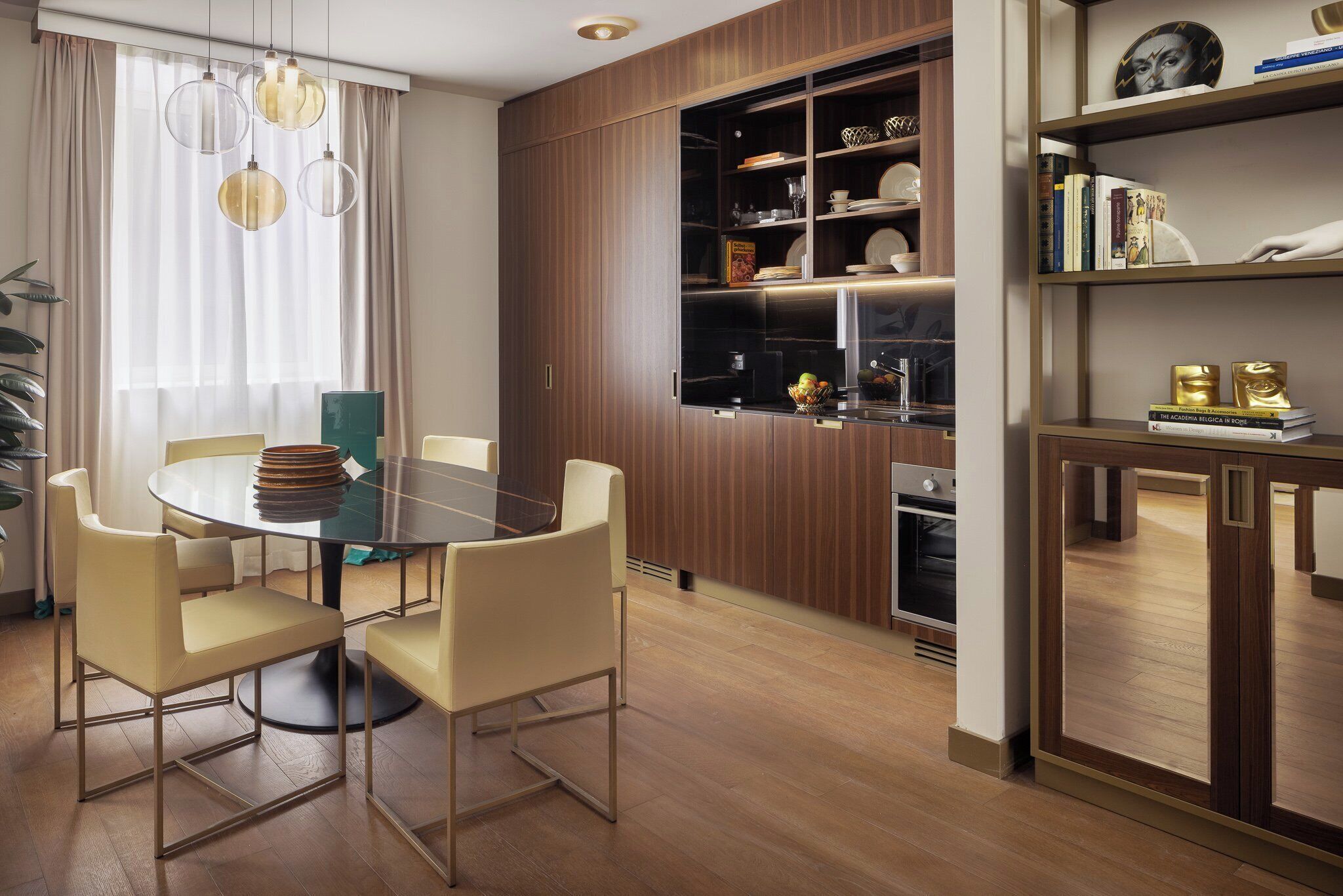 Een moderne eetruimte met een ronde glazen tafel, beige stoelen en een houten kast met planken.