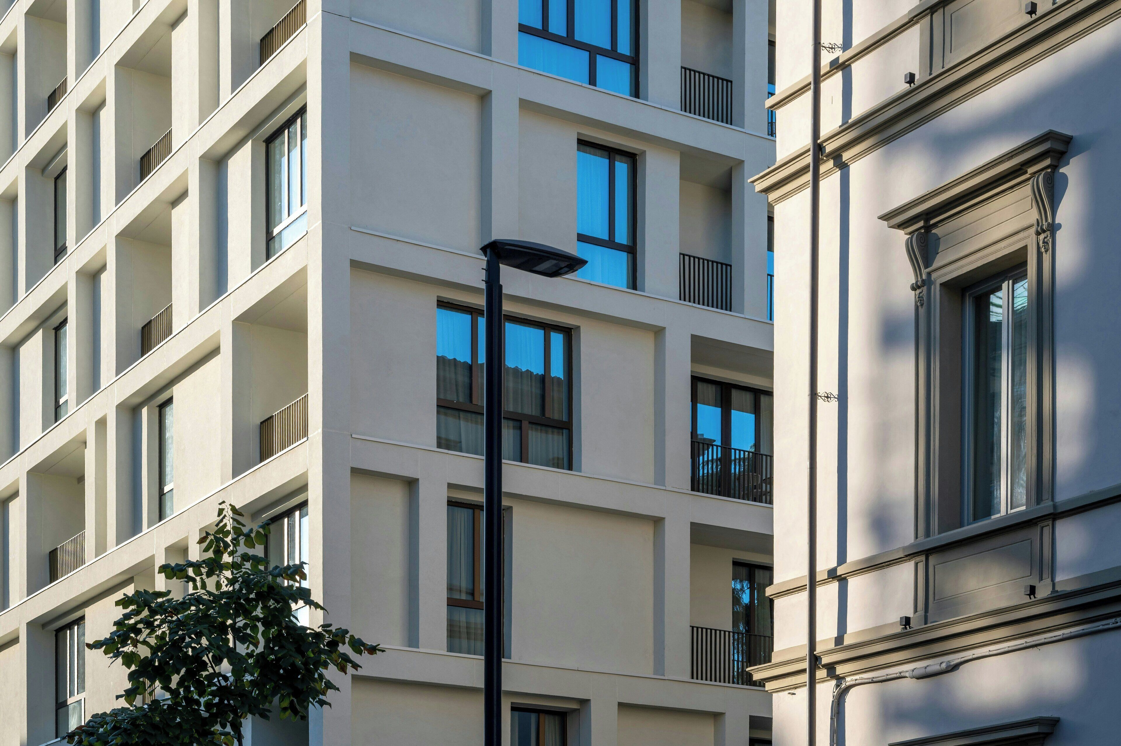 A multi-story building with balconies, a street lamp, and a tree in front.