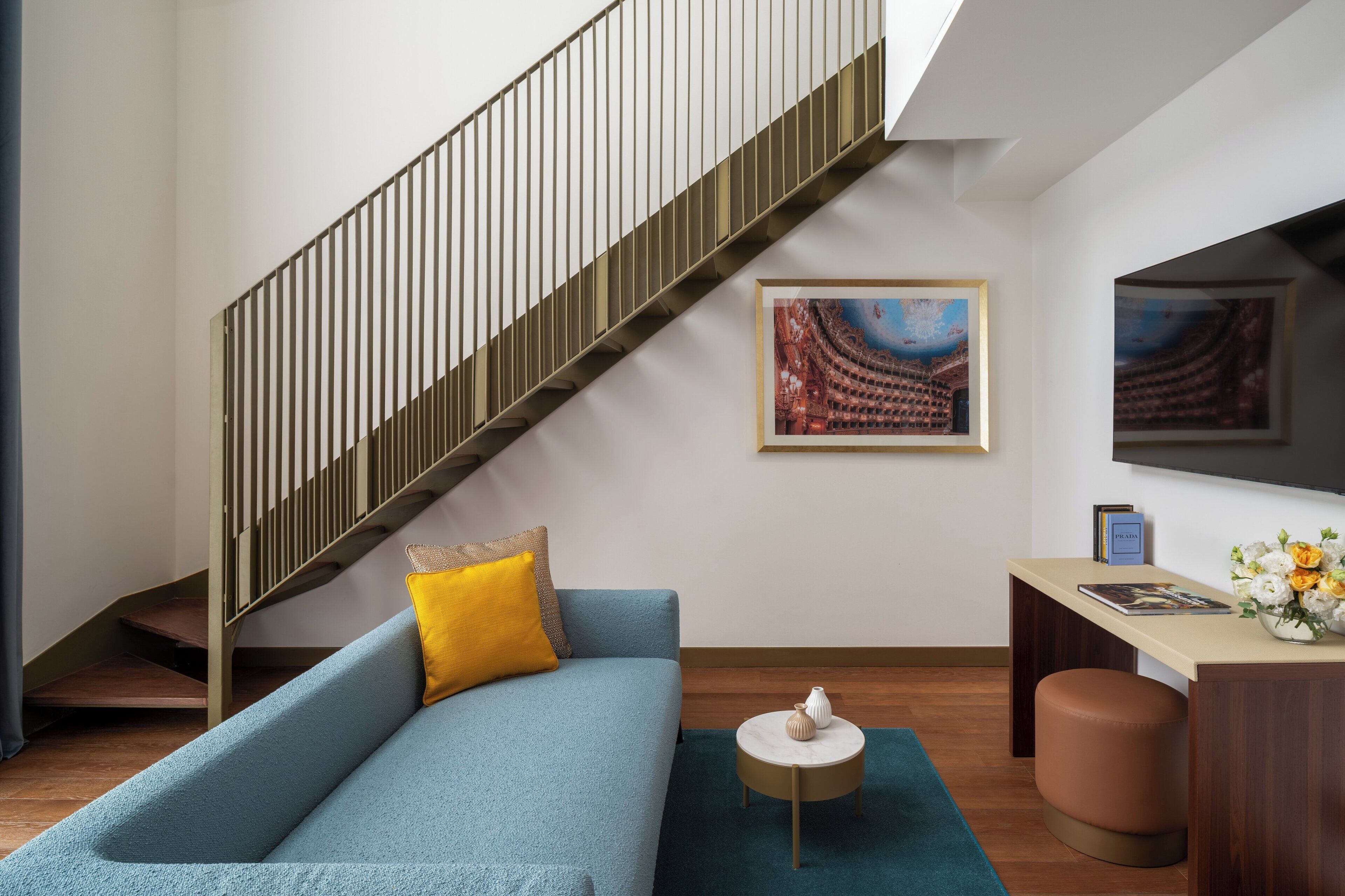 A modern living room with a blue sofa, a small round table, a wooden desk, and a staircase.