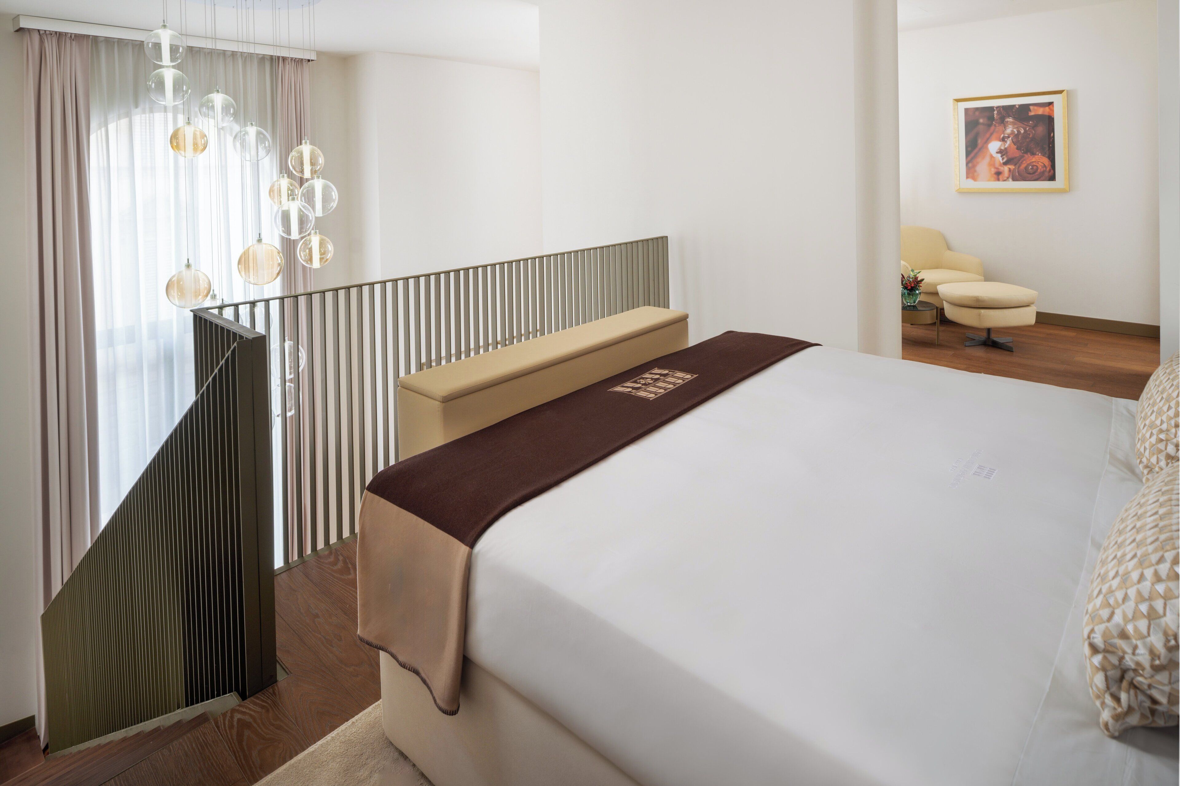 A hotel room with a bed, a bench, a chair, and a painting on the wall.