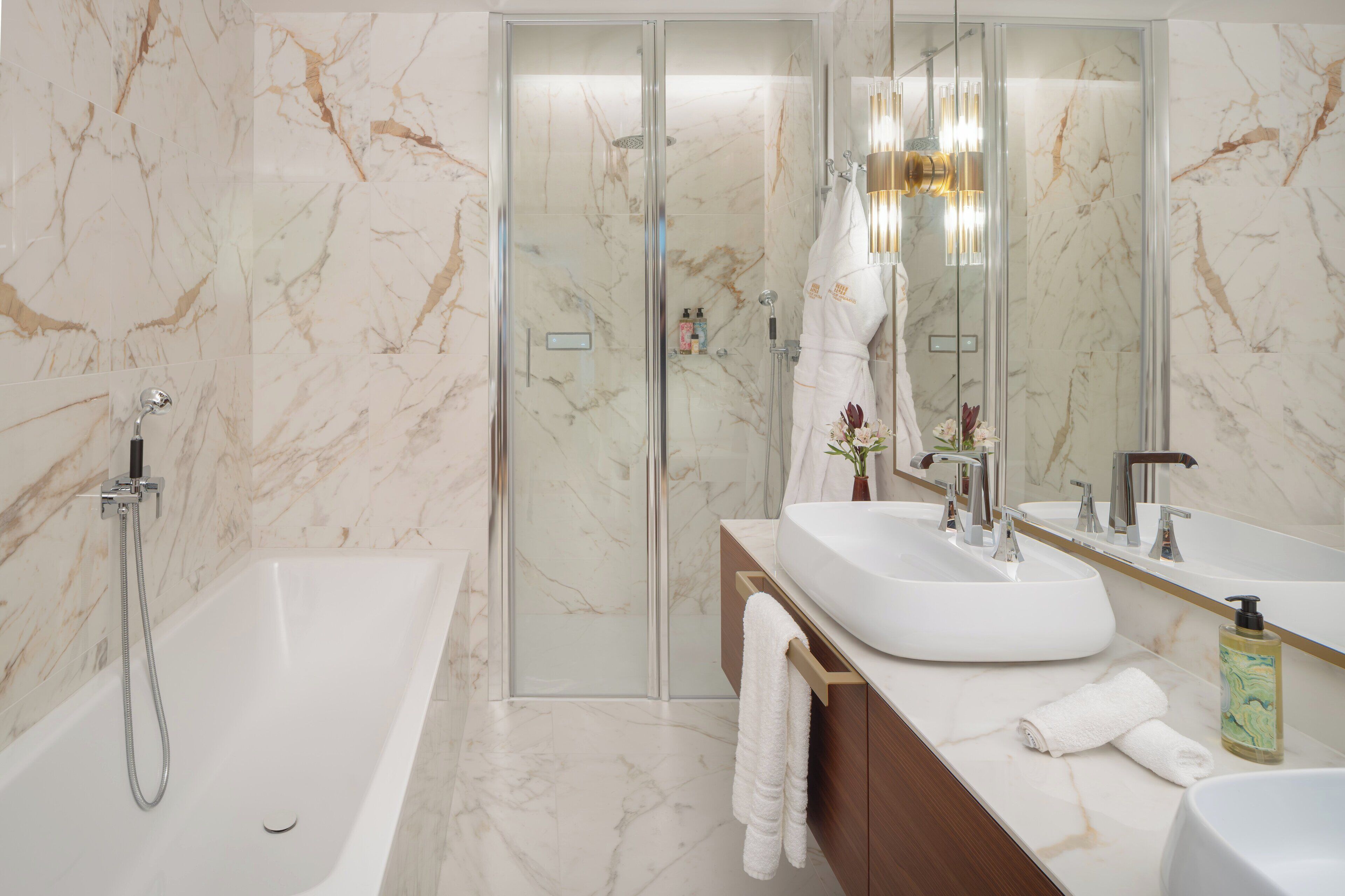 Un baño moderno con ducha de vidrio, una bañera blanca y un lavamanos doble con espejo.