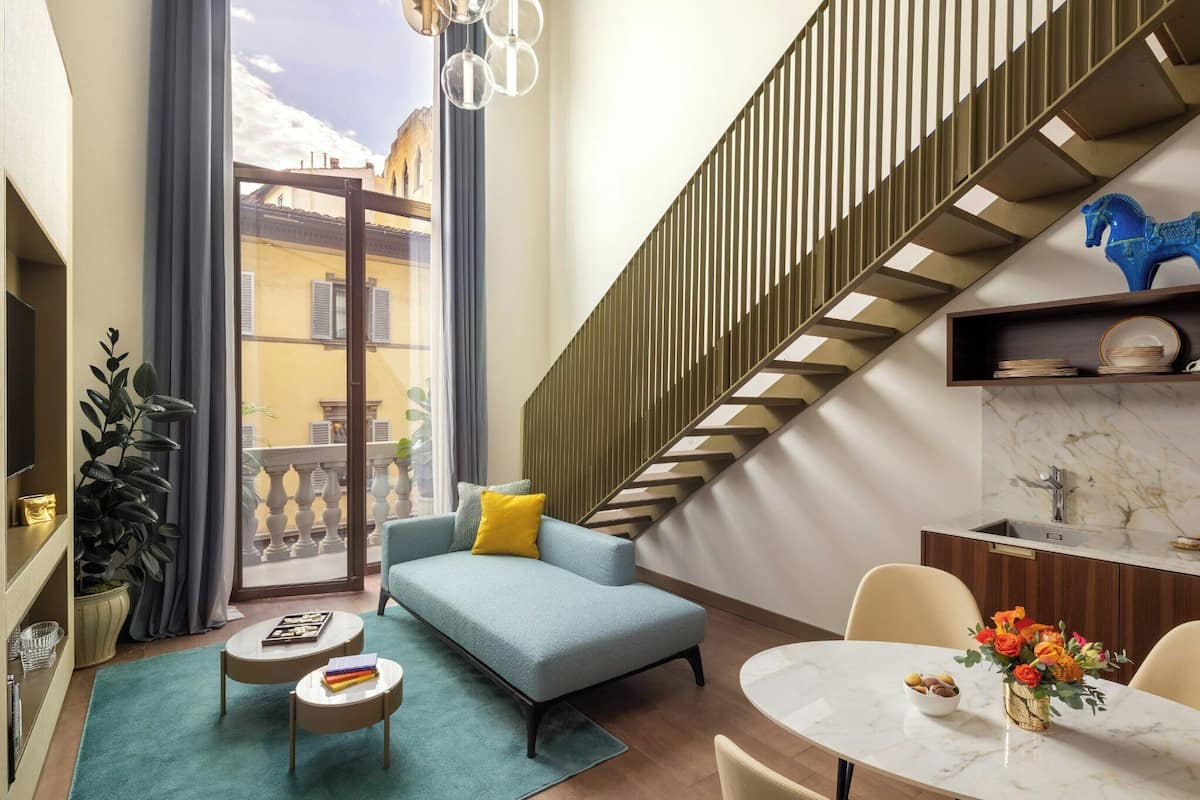 Una sala de estar moderna con un sofá azul, una mesa de comedor con un florero y una escalera decorada con un caballo azul.