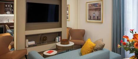 A modern living room with a flat-screen TV, a sofa, two armchairs, a small side table, and a coffee table.