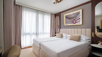 A hotel room with two beds, a large window with curtains, a framed picture on the wall, and a small table with a vase.