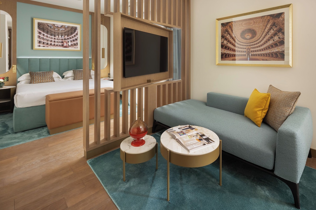 A hotel room with a bed, a TV, a sofa, and a small table with a globe and magazine.