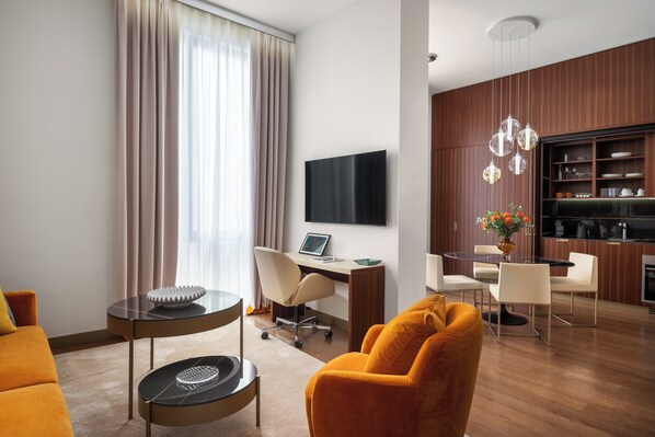Una habitación de hotel moderna con sofá, escritorio con computadora portátil, comedor y televisor montado en la pared.