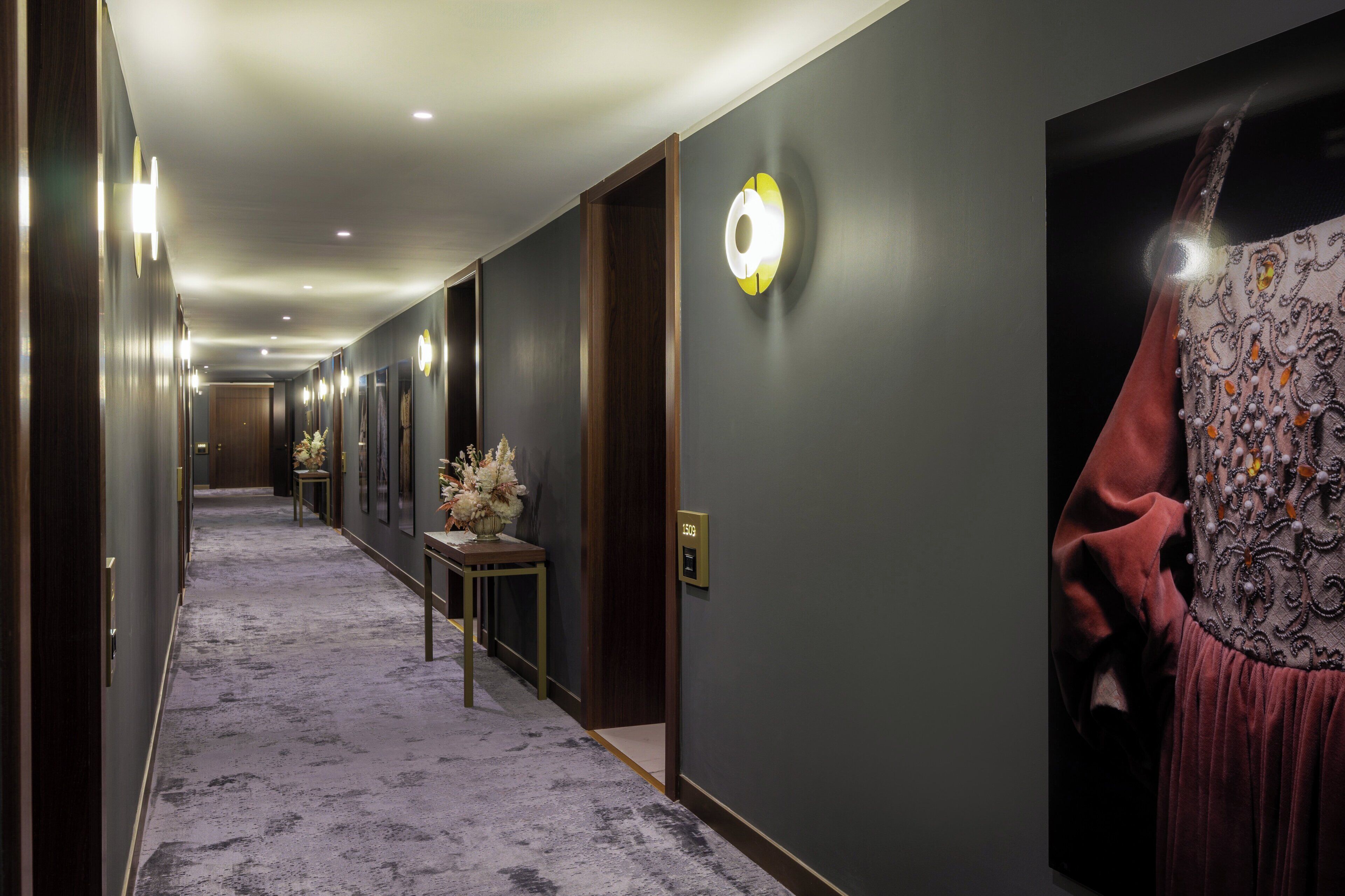 A hotel corridor with a carpeted floor, framed artwork on the walls, and a door with a number plate.