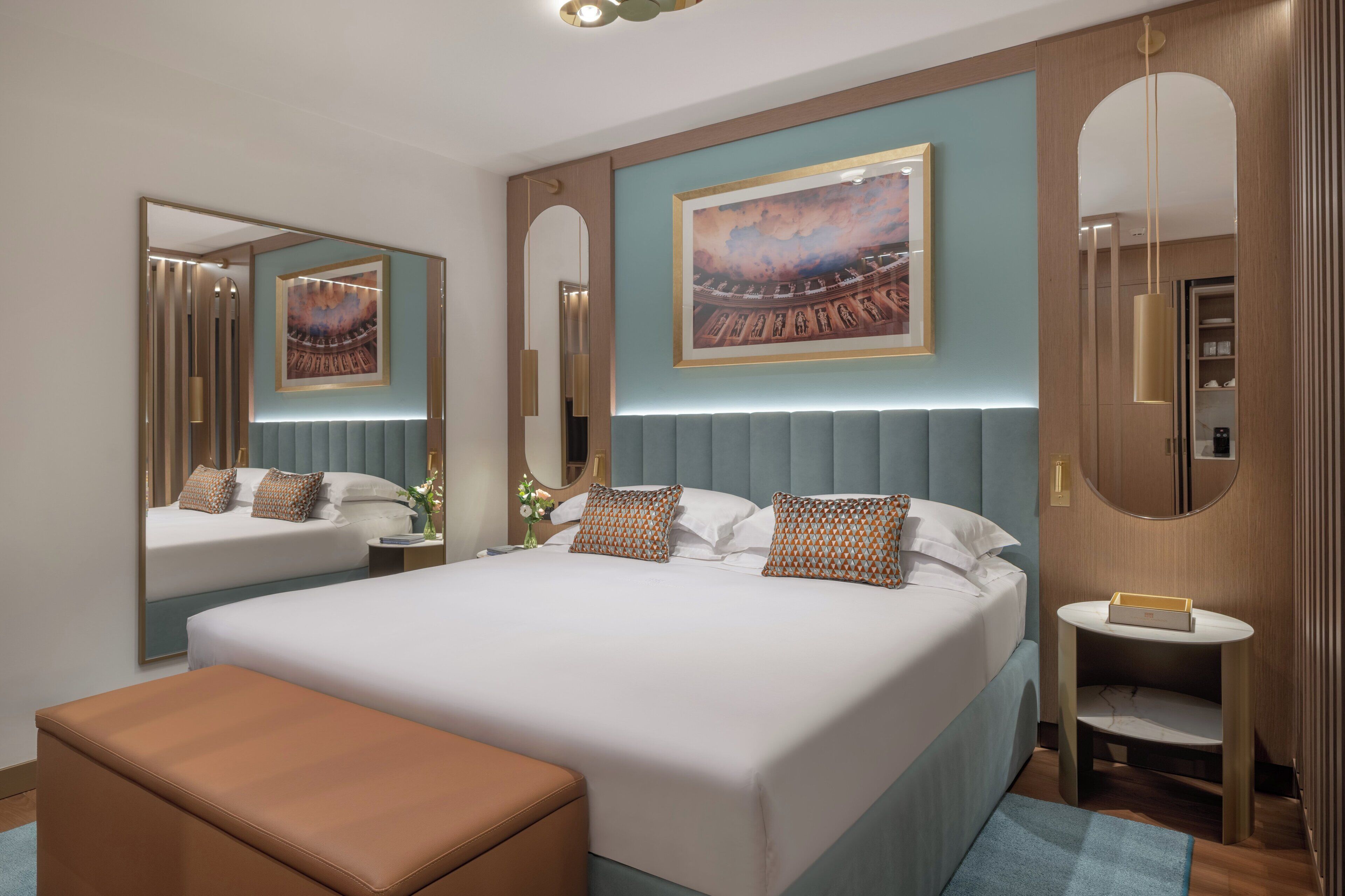 Una habitación de hotel moderna con una cama grande, una mesita de noche, un espejo y una obra de arte colgada en la pared.
