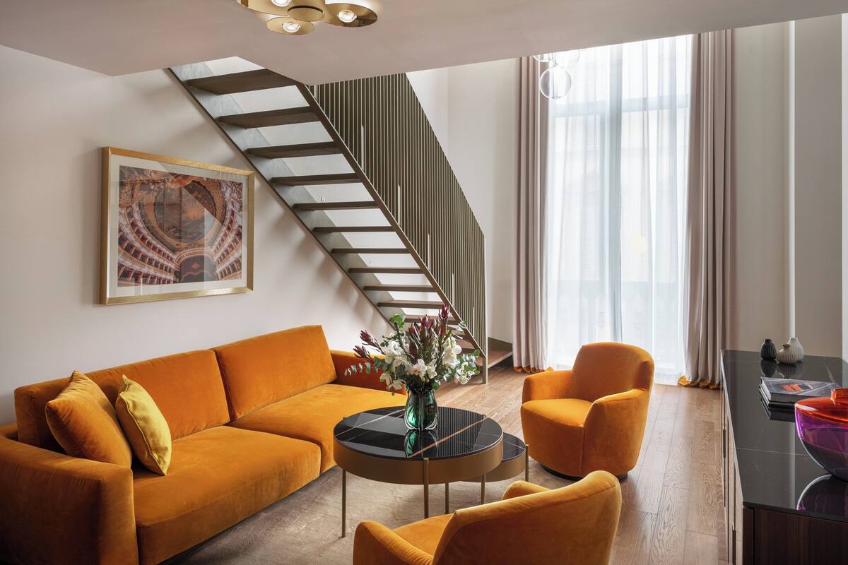 A modern living room with a sofa, armchairs, a coffee table, and a staircase.