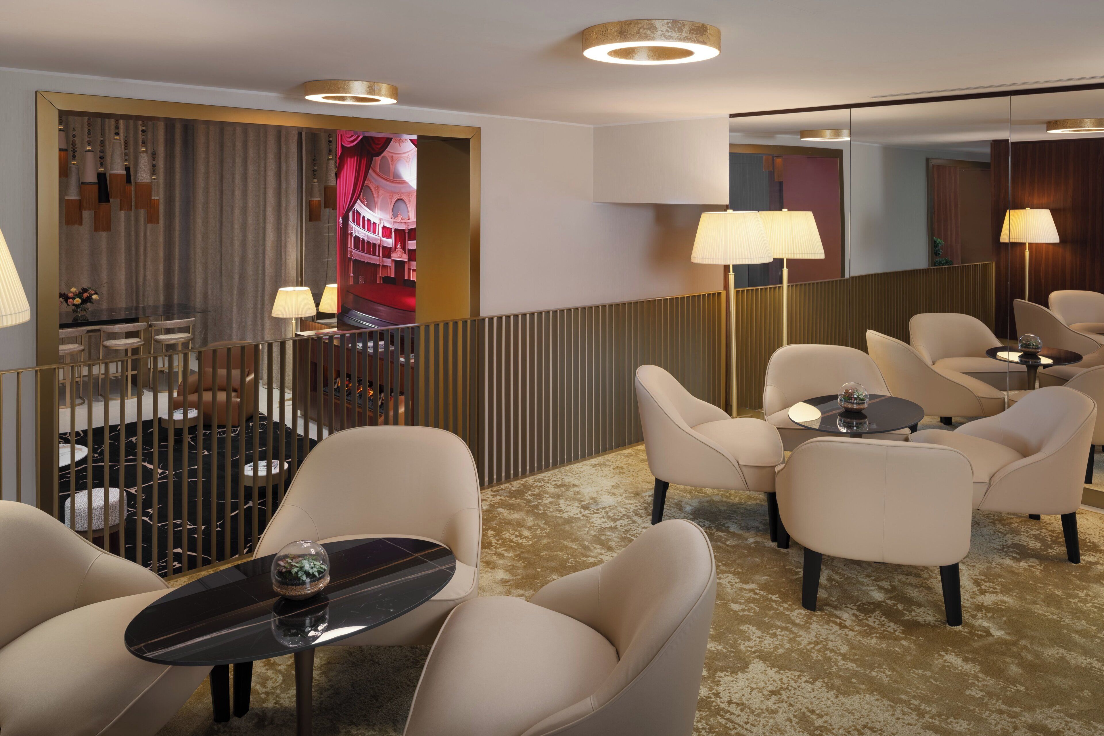 Un hall d’hôtel doté d’un espace salon avec des canapés et une petite table ronde, d’un bar avec un comptoir et des tabourets, et d’un grand miroir qui reflète l’intérieur.