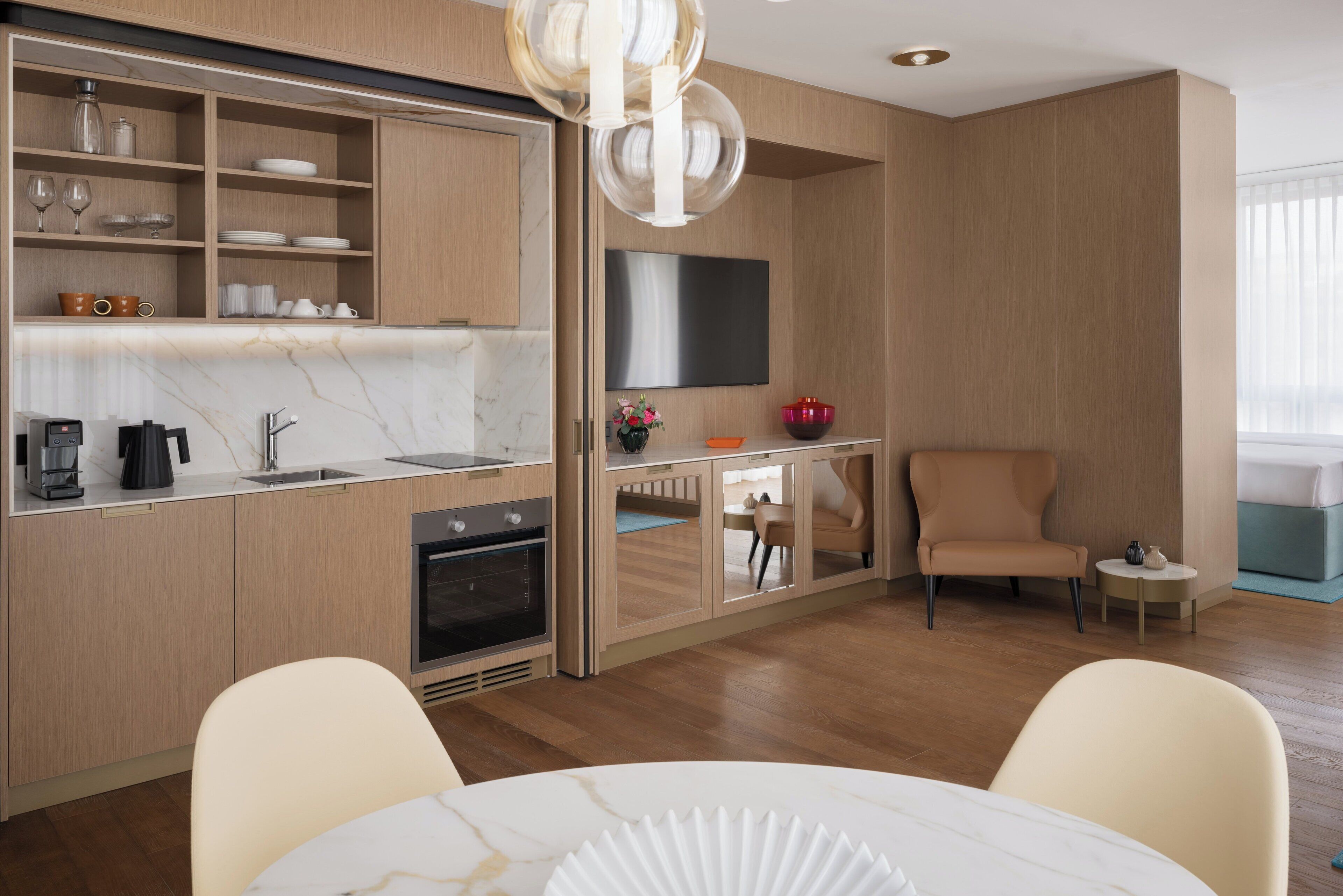 Una cocina moderna con electrodomésticos integrados, una zona de comedor con mesa de mármol y un rincón con una silla y una mesita.