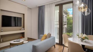 A modern living room with a flat-screen TV, a sofa, a dining table with chairs, and a balcony with curtains.