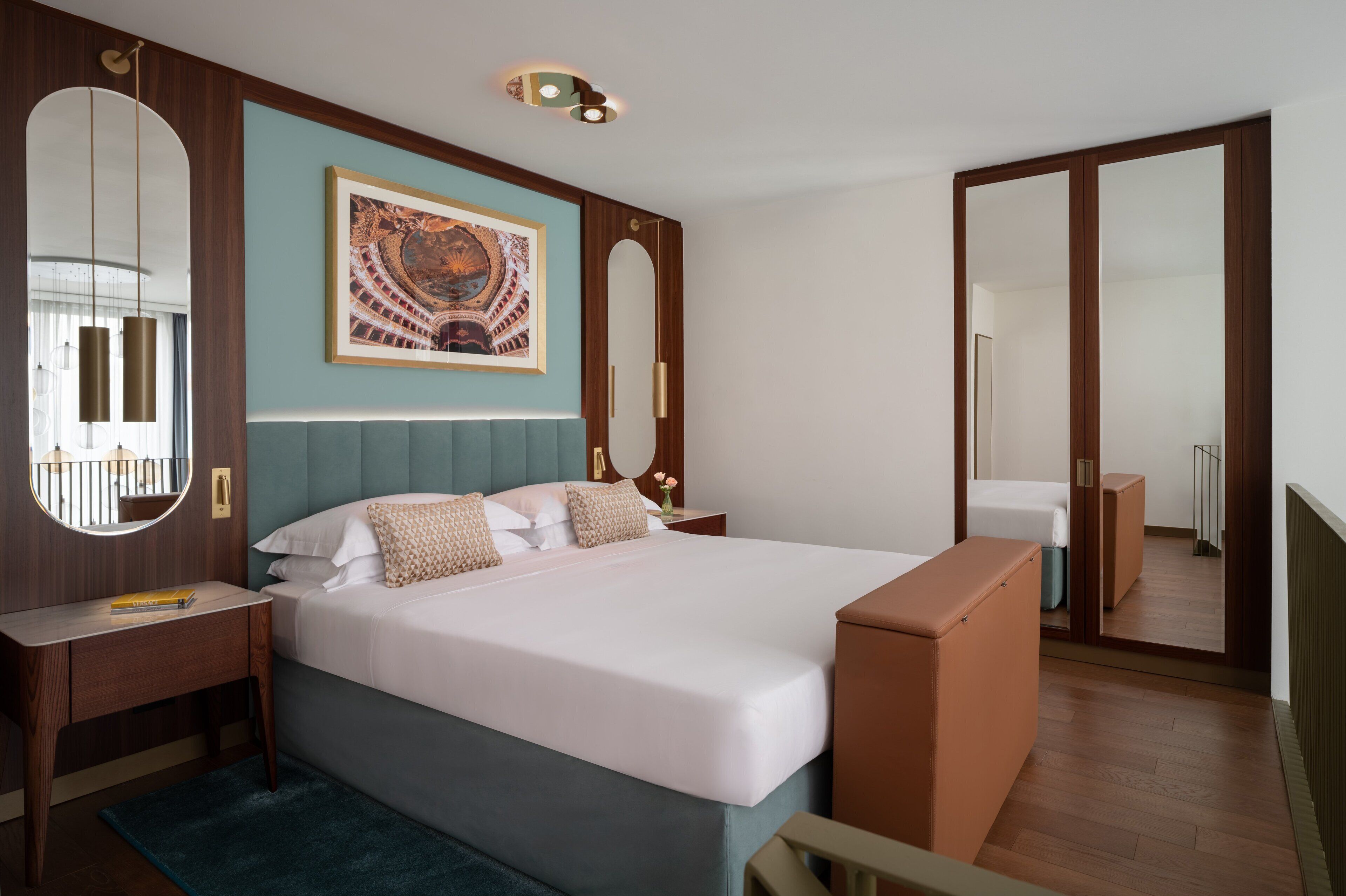 A modern hotel room with a large bed, a desk, a mirror, and a wardrobe.