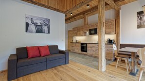 Una cocina moderna con armarios de madera, microondas integrado y cafetera. En la sala de estar, hay un sofá gris con cojines rojos.