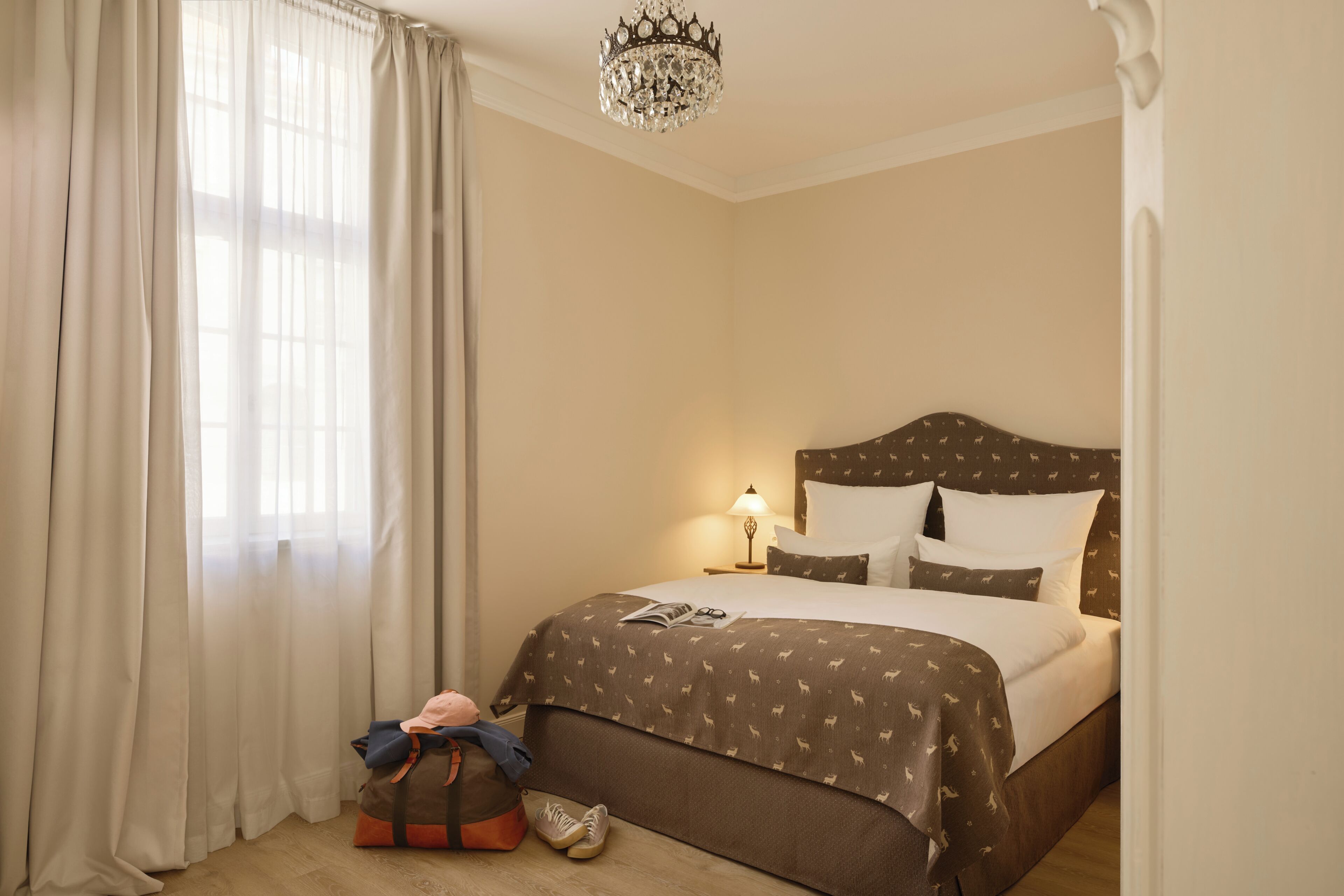Ein Hotelzimmer mit Bett, Nachttisch, Lampe, Koffer und einer Kristallleuchtre.