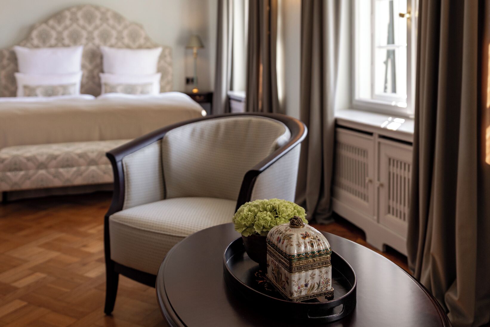 A hotel room with a bed, a chair, a small table with a decorative item, and a window with curtains.