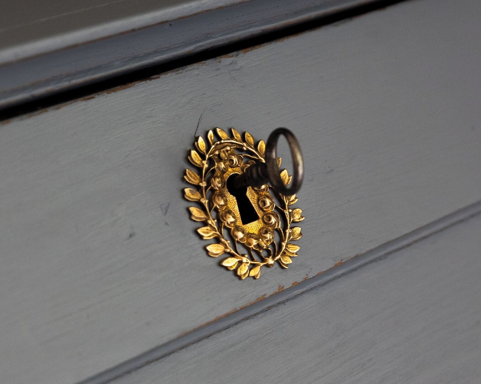 A close-up of a brass door handle with a keyhole, surrounded by a decorative floral pattern.
