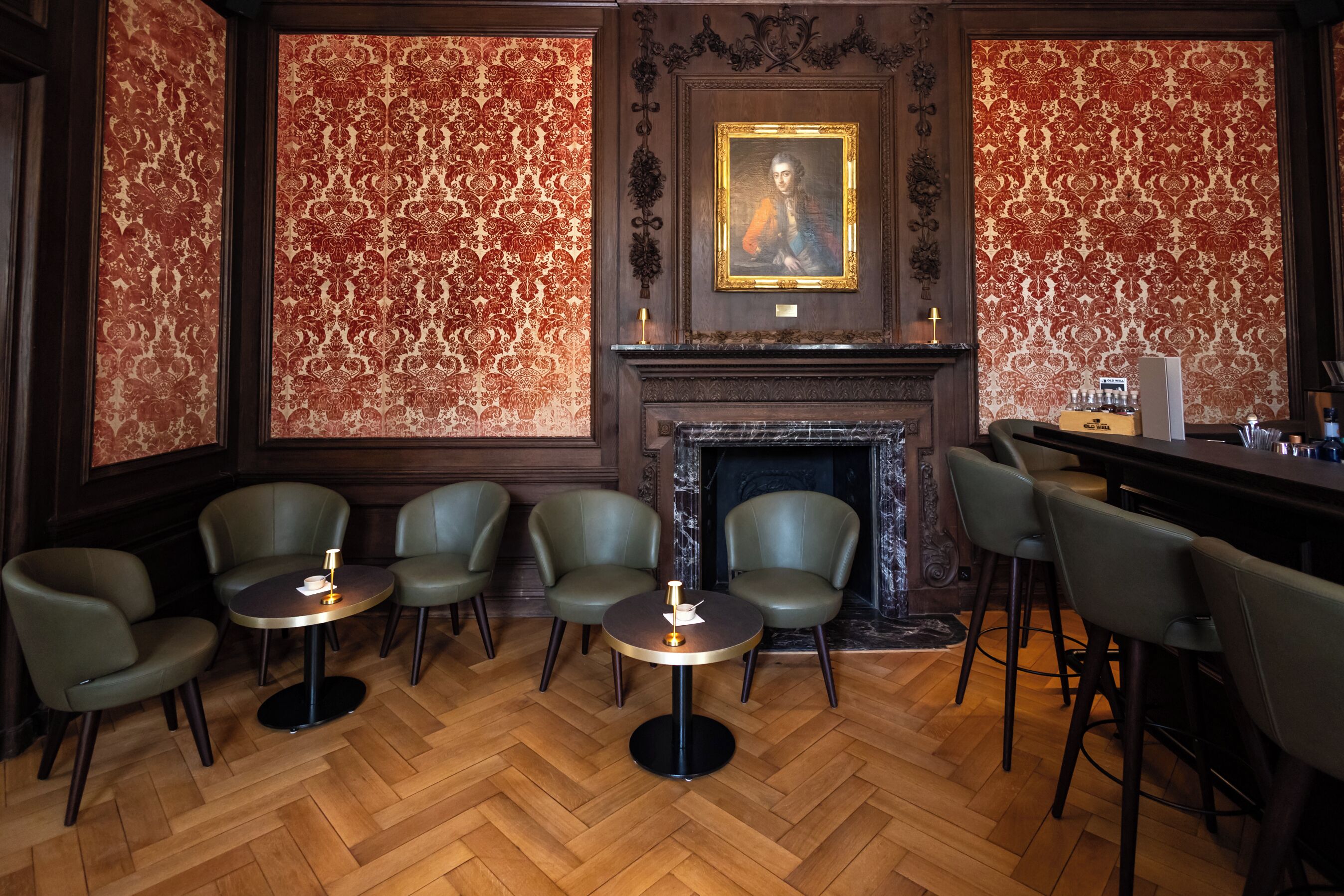 A bar area with a fireplace, patterned wallpaper, and leather chairs.