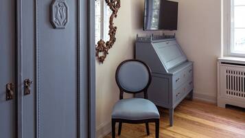 A room with a wooden floor, a grey dresser, a chair, a mirror, and a television mounted on the wall.