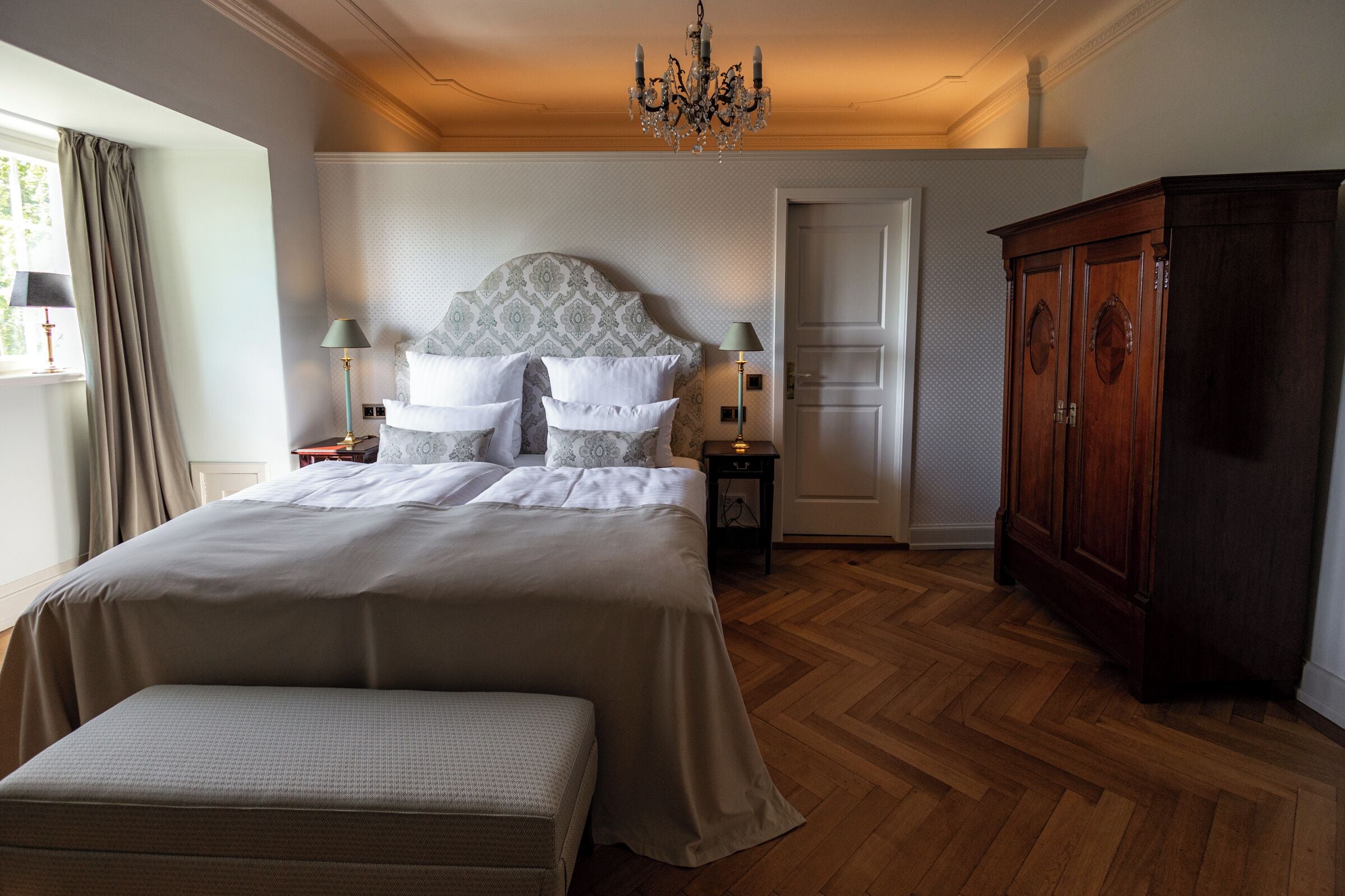 A bedroom with a large bed, a wooden floor, a chandelier, and a wardrobe.